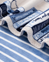 A close-up of a folded fabric item, likely a towel or blanket, featuring a blue and white striped pattern with printed text and decorative bands, layered over a matching blue and white striped textile.