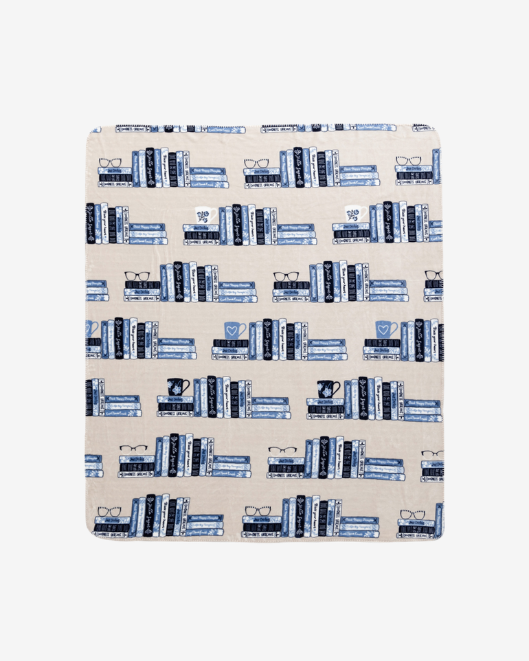 A rectangular fabric blanket, featuring a repeating pattern of blue and navy bookshelves with books on a warm beige background.