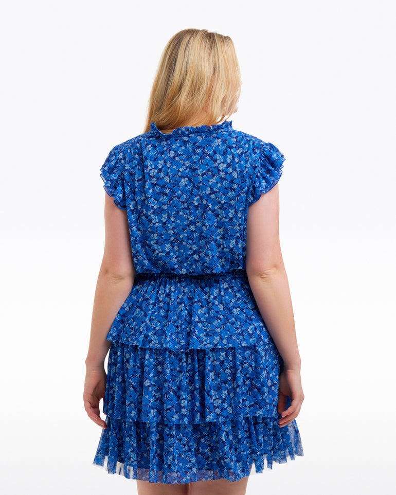 A woman with blonde hair is shown from the back wearing the Draper James Alana Tiered Dress in Blue Scattered Ditsy against a plain white background.