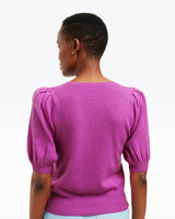 A person with short hair is seen from behind wearing the Draper James Short Sleeve Cashmere Sweater in purple with puffed shoulders and light blue jeans, set against a plain white background.