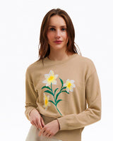 A woman wears the Draper James Daffodil Crewneck Sweater, which features a white and yellow embroidered floral design, standing against a plain white background.