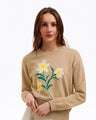 A woman wears the Draper James Daffodil Crewneck Sweater, which features a white and yellow embroidered floral design, standing against a plain white background.