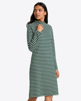 A woman stands against a plain background wearing the Draper James Elsie Turtleneck Dress in Green Stripe, featuring long sleeves and a high neckline.