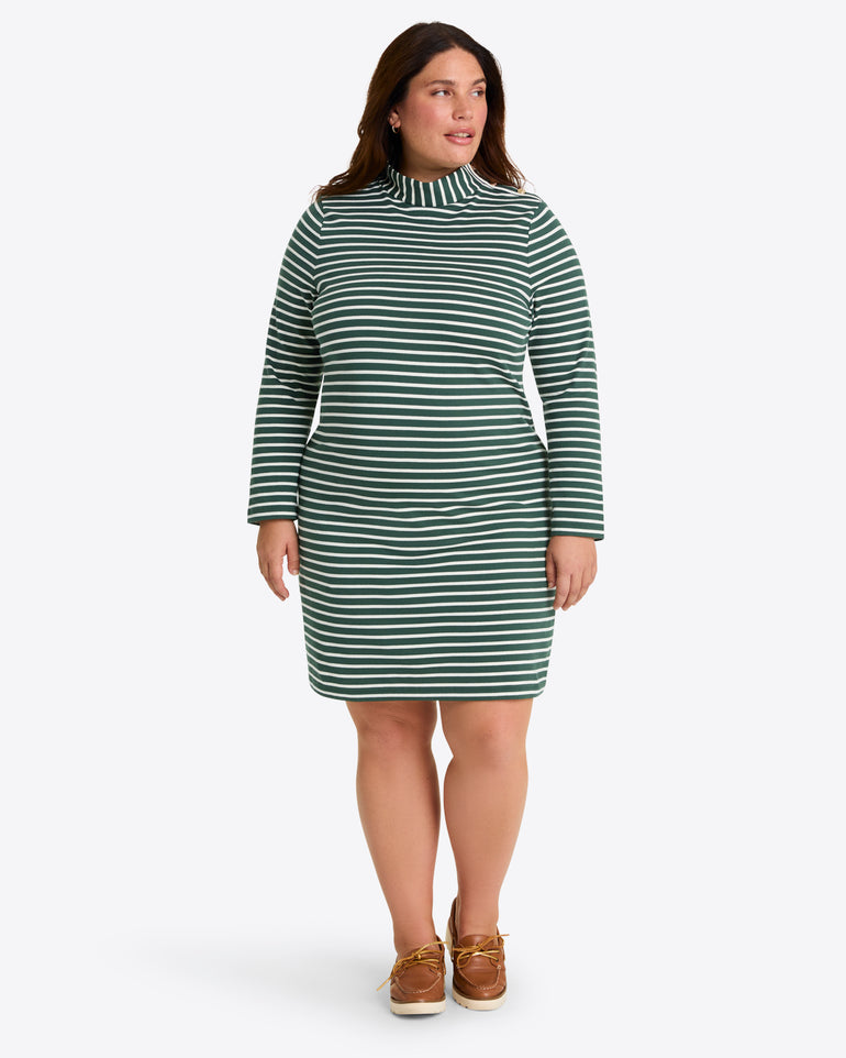 A woman wears the Draper James Elsie Turtleneck Dress in Green Stripe, paired with brown boat shoes, standing against a plain light background.