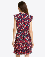 A woman with long brown hair is shown from the back wearing the Draper James Alana Tiered Dress in Stretch Mesh, featuring a navy blue, red, and white floral print with ruffled sleeves and a tiered skirt.
