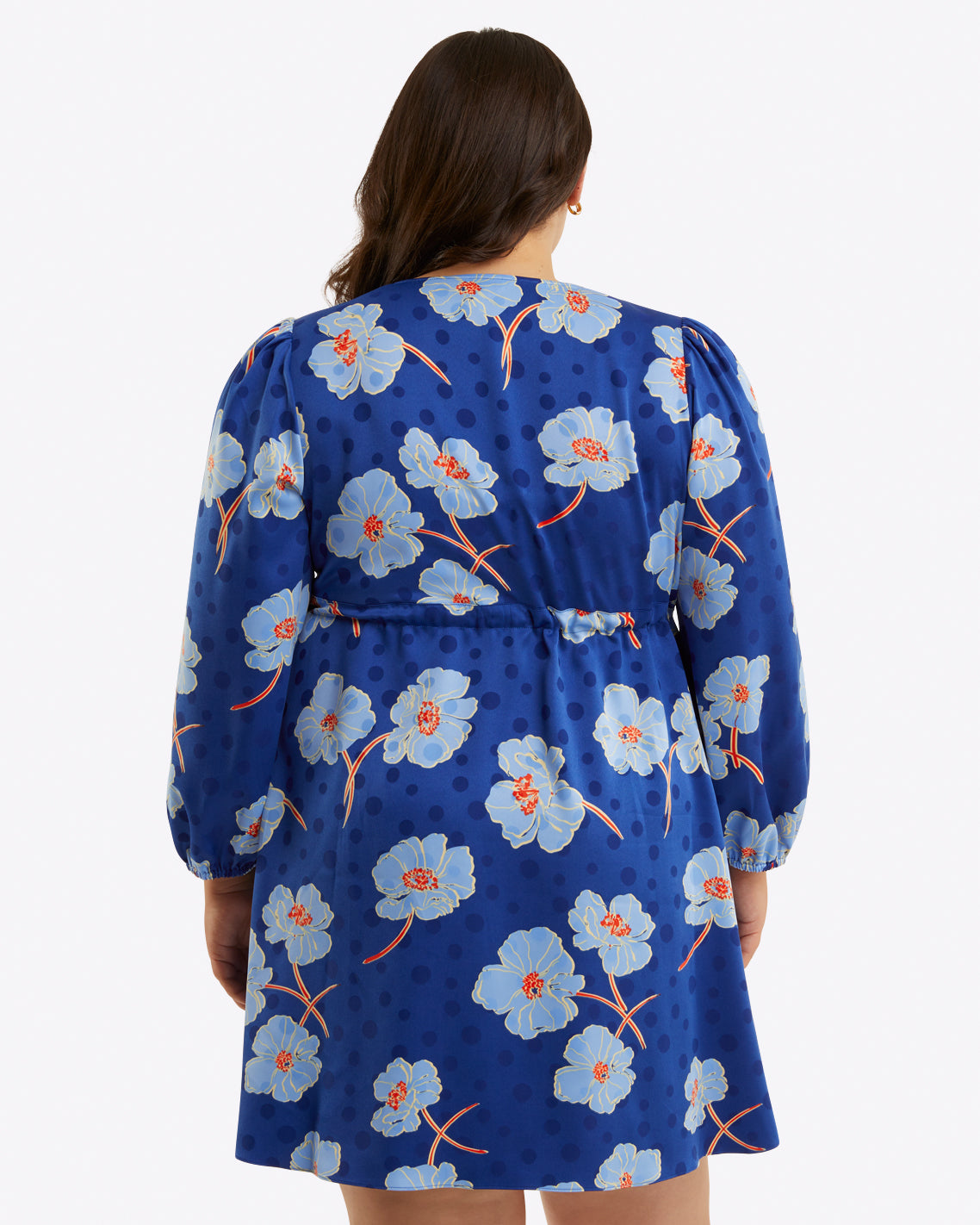 A woman is shown from the back wearing the Draper James Kellie Babydoll Dress in Printed Dot Jacquard, featuring a blue v-neck, long sleeves, and a light blue floral pattern, set against a plain background.