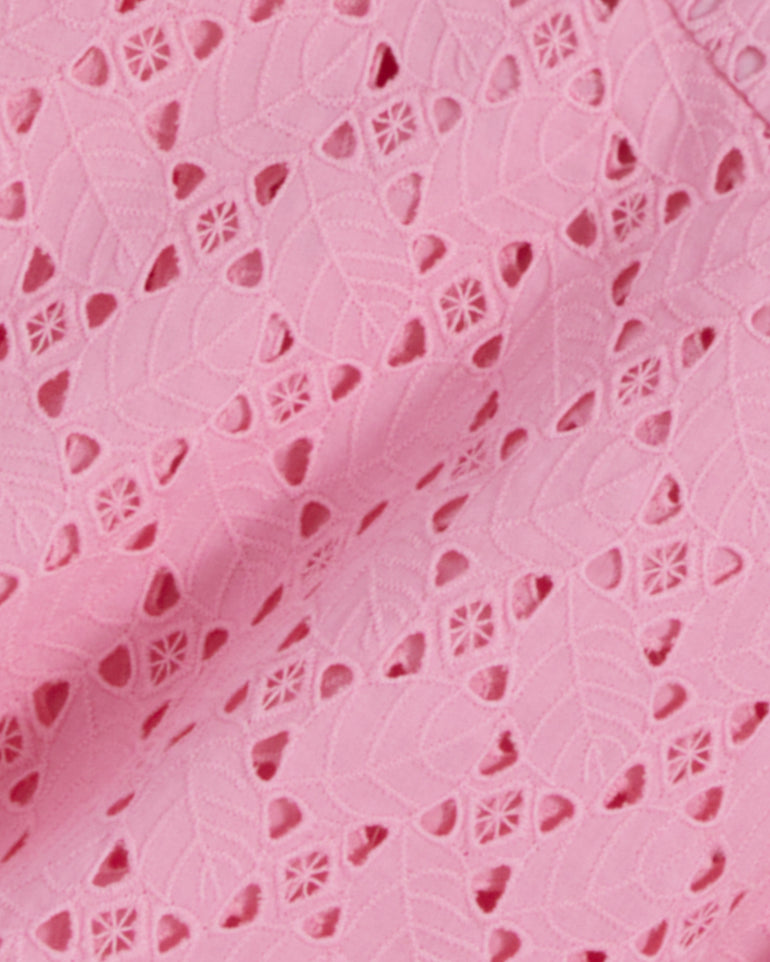 The Caitlyn Midi Dress in Eyelet by Draper James features a close-up of pink lace fabric with a leaf and floral cutout pattern. It has a square neckline and is crafted from delicate cotton eyelet for an elegant touch.