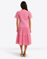 A person stands facing away, wearing the Draper James Caitlyn Midi Dress in pink cotton eyelet, featuring a square neckline, short sleeves, and a tiered skirt.