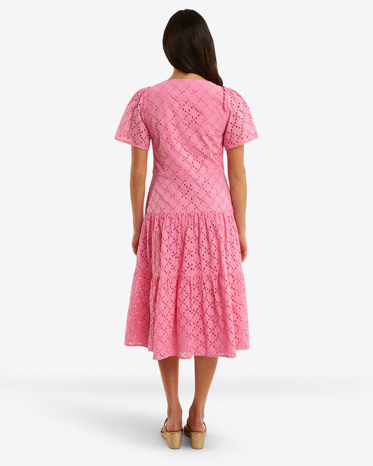 A person stands facing away, wearing the Draper James Caitlyn Midi Dress in pink cotton eyelet, featuring a square neckline, short sleeves, and a tiered skirt.