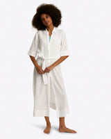 A woman stands barefoot in the Draper James Crinkle Cotton Coverupâ€”a white button-down beach dress with a removable belt and three-quarter sleevesâ€”against a plain background.
