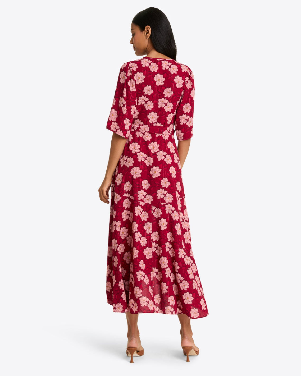 A woman faces away, wearing the Draper James Fiona Wrap Midi Dress in Lurex Crepe with a red and pink floral print, short sleeves, and a high-low hem, paired with beige heels. This style is also available in plus sizes.