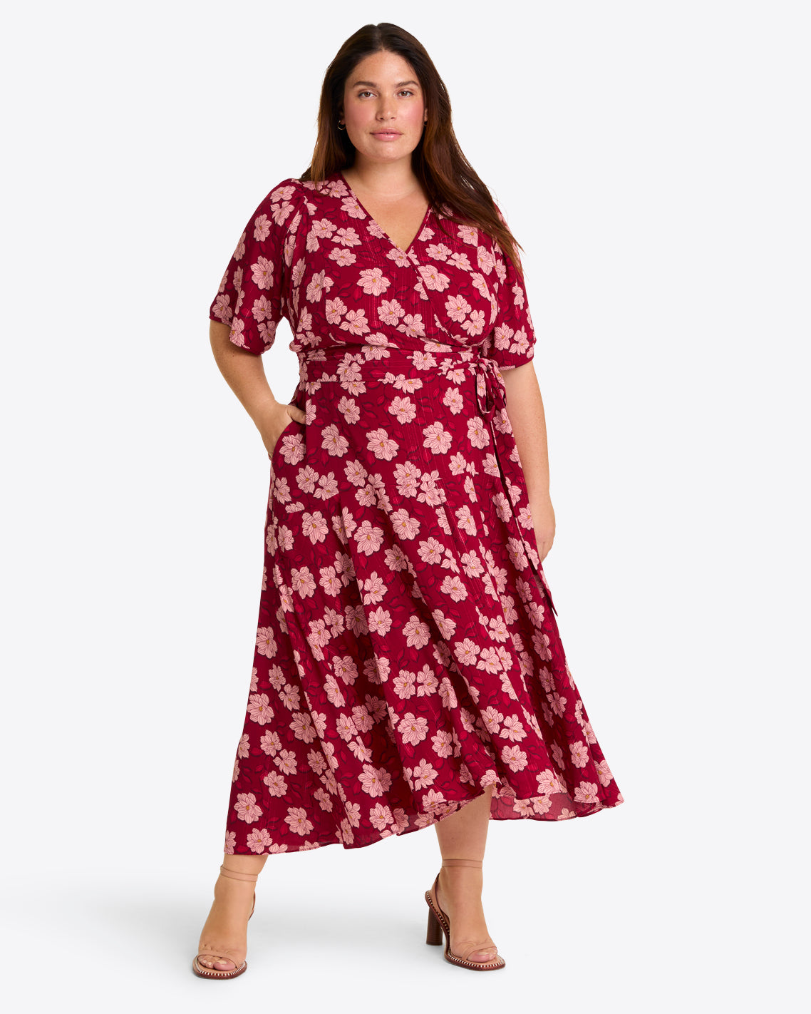 A woman wears the Draper James Fiona Wrap Midi Dress in Lurex Crepe—a red, short-sleeve, floral wrap dress with a high-low hem and tie waist—paired with tan heeled sandals against a plain light background.
