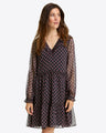 A woman wears the Draper James Lorrie Long-Sleeve Dress in Crinkle Chiffonâ€”a black, V-neck dress with pink and white diamond print, ruffled hem, and long sleevesâ€”standing against a plain background.