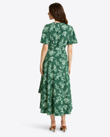 A woman faces away, wearing the Draper James Gigi Wrap Dressâ€”a green, floral, short-sleeve plus-size midiâ€”and tan heeled sandals.