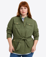 A person wears the Draper James Field Jacket in Green Twill, featuring a belted waist and buttoned chest pocketsâ€”an ideal pick for fall style against a plain background.