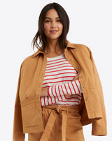 A person in a Draper James Utility Jacket in Cotton Twill over a red and white striped shirt, paired with matching tan pants, stands against a plain background.