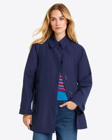 A person wearing a Draper James Button Front Coat in navy blue over a colorful sweater and blue jeans stands against a plain light background.