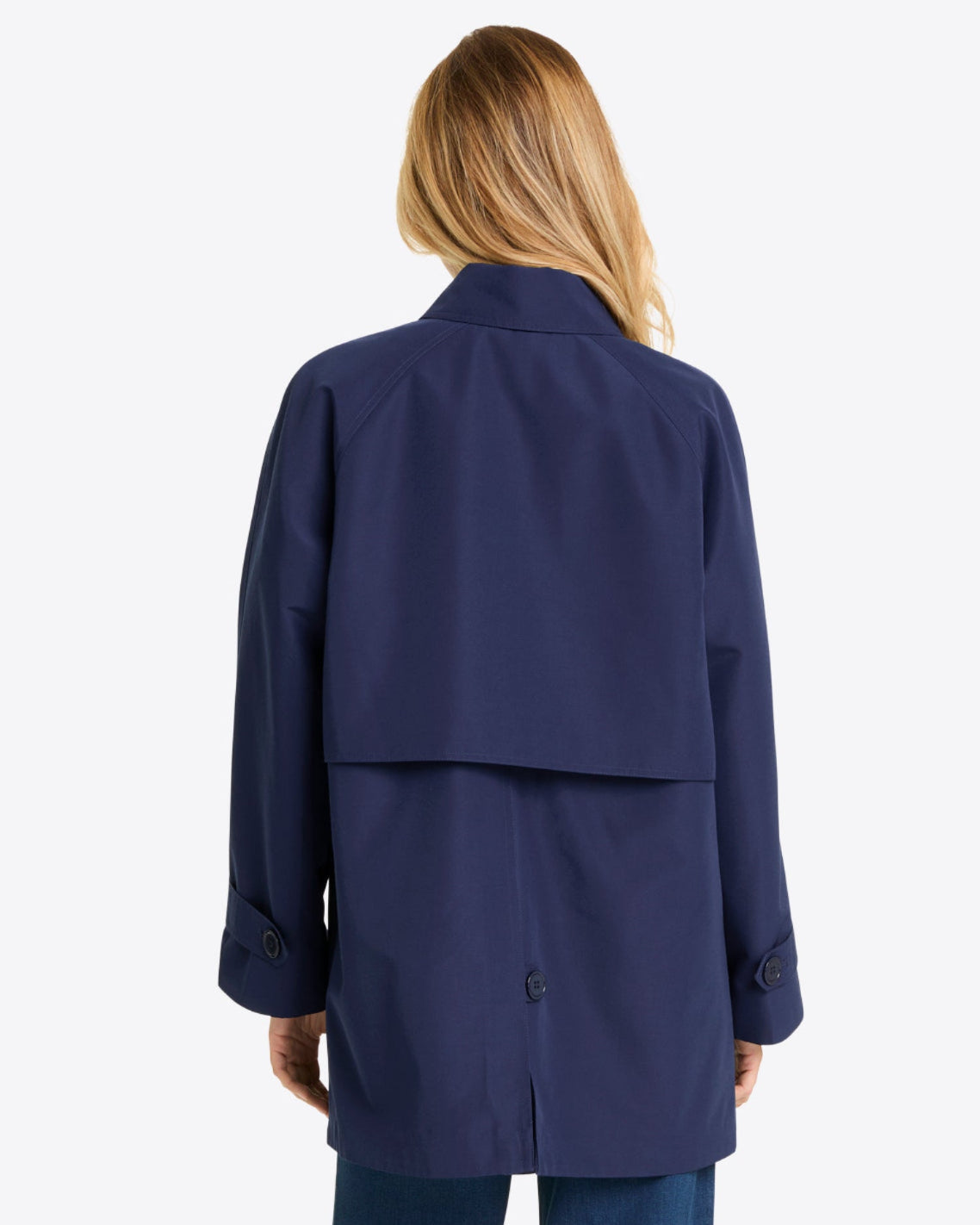 A person with long, blonde hair is shown from the back, wearing a Draper James Button Front Coat in navy blue and blue jeans, set against a plain light background.