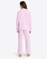 Wearing the Linda Pajama Set in pink and white striped 100% cotton, the person stands barefoot with their back to the camera, highlighting the comfort of its elastic waist pants.