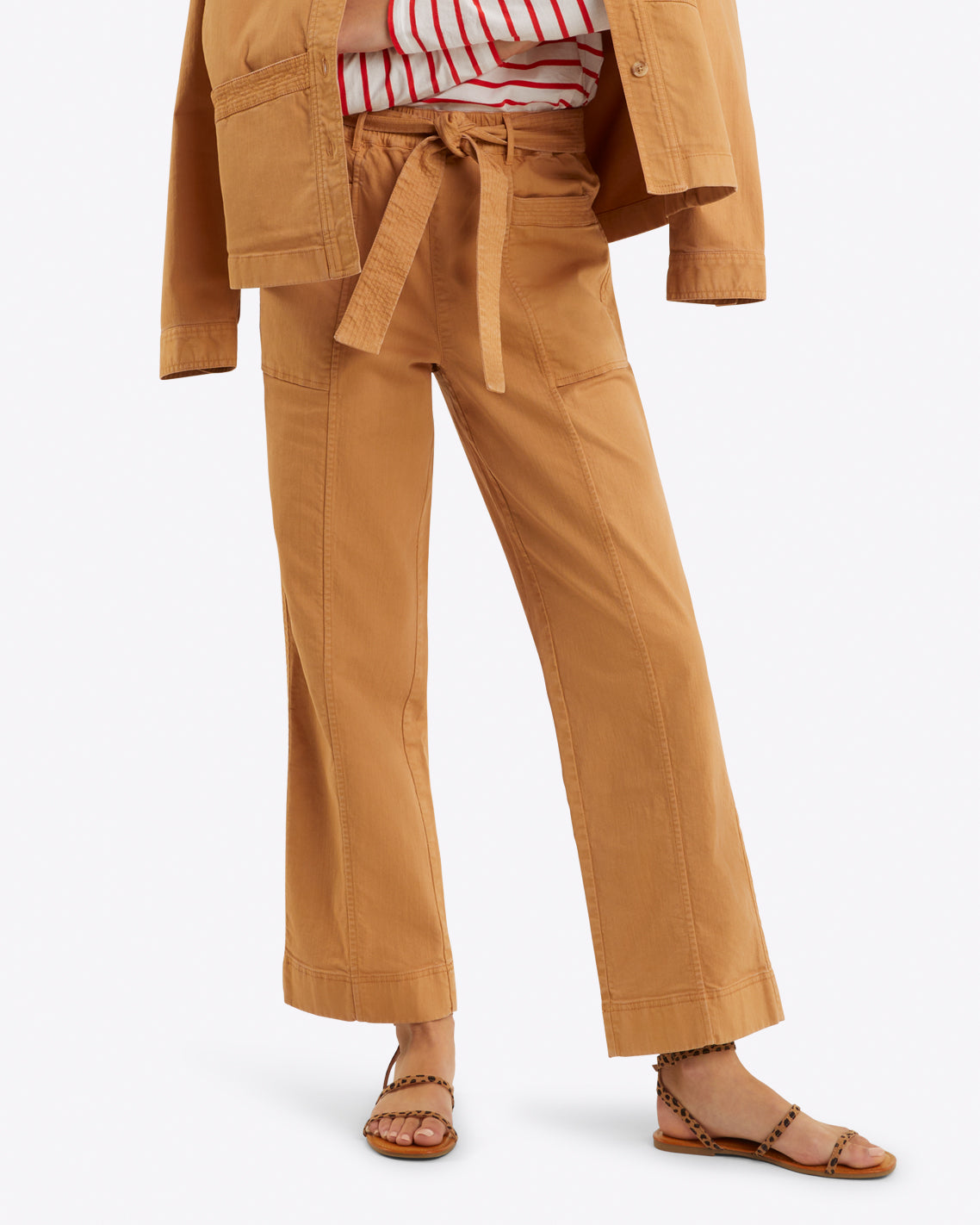 The person in a brown Utility Pant in Cotton Twill by Draper James and matching jacket looks effortlessly stylish. Tied at the waist over a red and white striped shirt, the outfit is completed with brown sandals for a chic yet comfortable look.