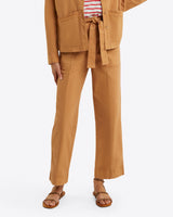 A person is styled in a tan ensemble from Draper James, featuring a belted jacket, relaxed-fit Utility Pant in Cotton Twill, a striped shirt, and sandals on a white background.