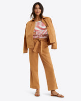A person models Draper James' Utility Jacket in Cotton Twill with matching pants over a striped shirt, smiling in sandals, perfect for spring layering against a simple backdrop.