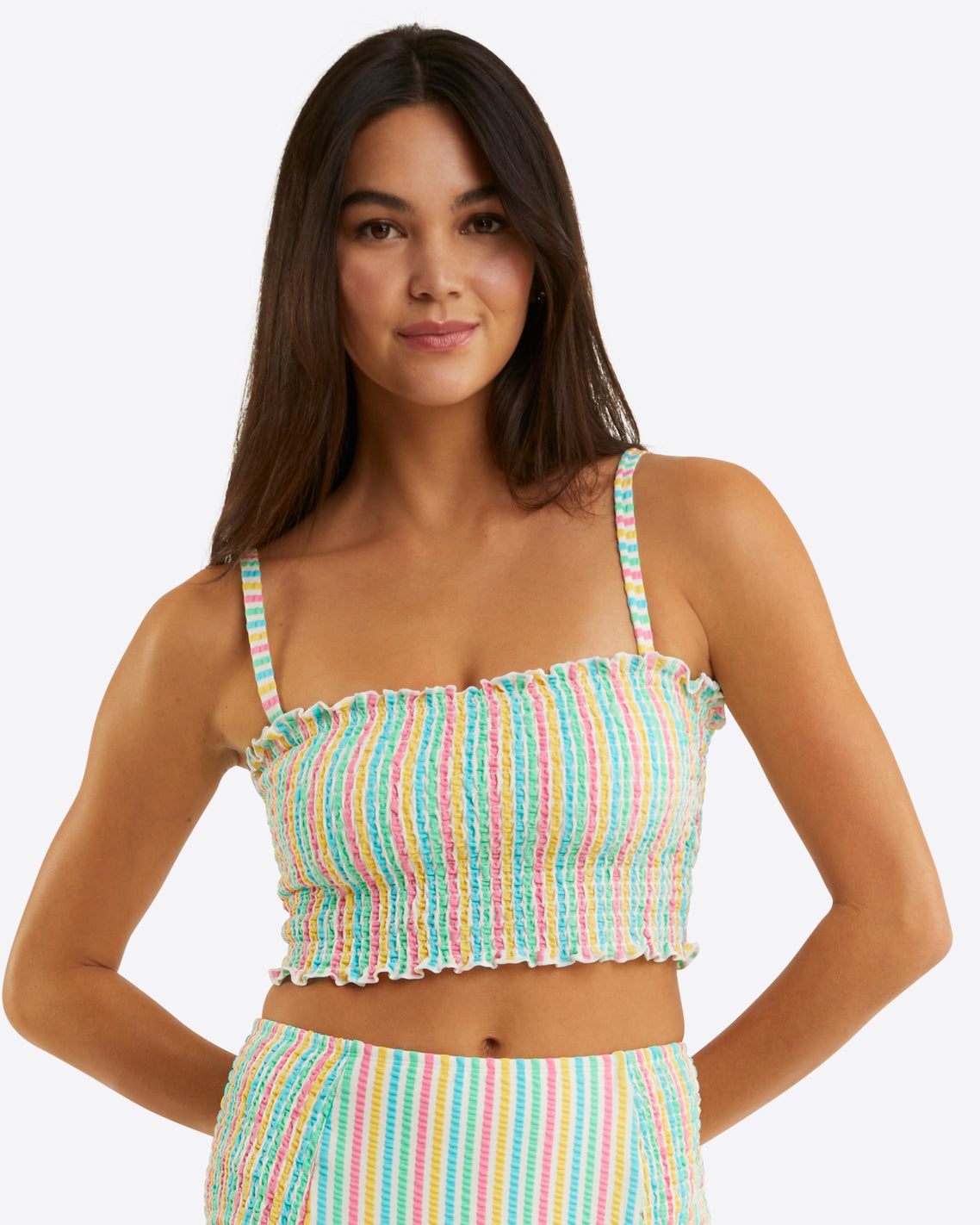 A woman with long dark hair wears the Draper James Smocked Bikini Topâ€”colorful, striped, with thin strapsâ€”paired with matching high-waisted bottoms against a plain light background. This seersucker set combines comfort and sunny-day style.