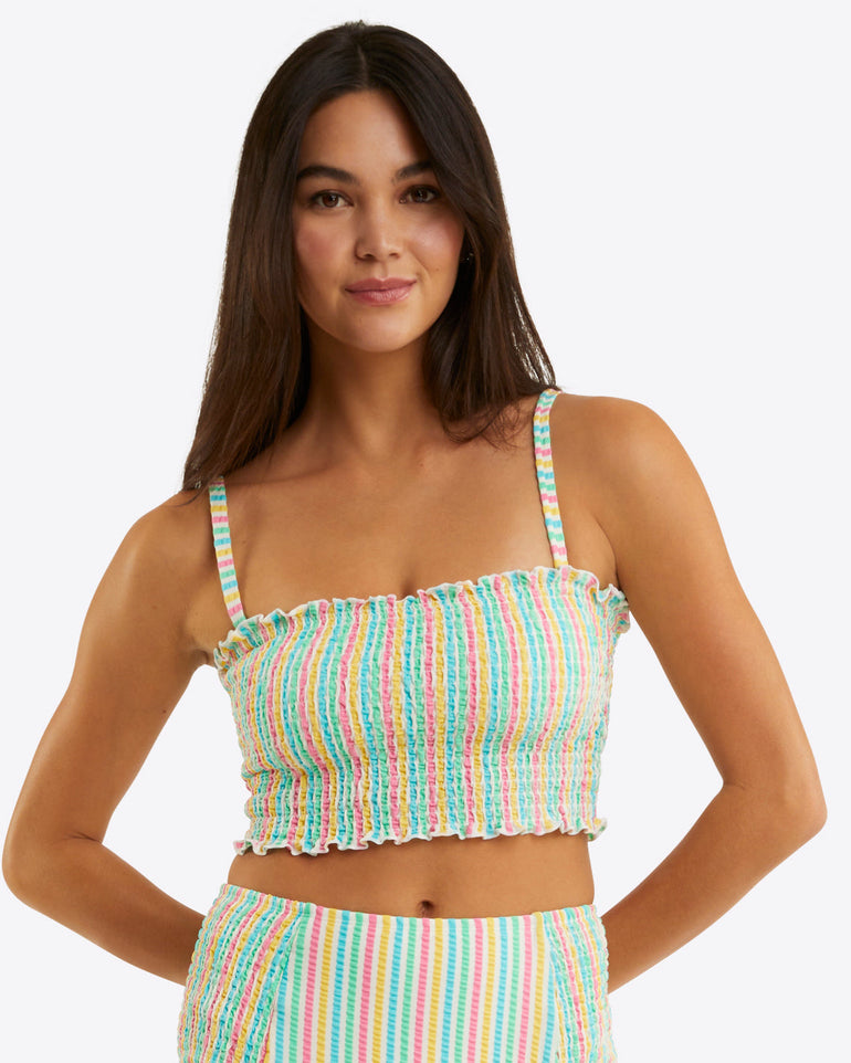 A woman with long dark hair wears the Draper James Smocked Bikini Topâ€”colorful, striped, with thin strapsâ€”paired with matching high-waisted bottoms against a plain light background. This seersucker set combines comfort and sunny-day style.