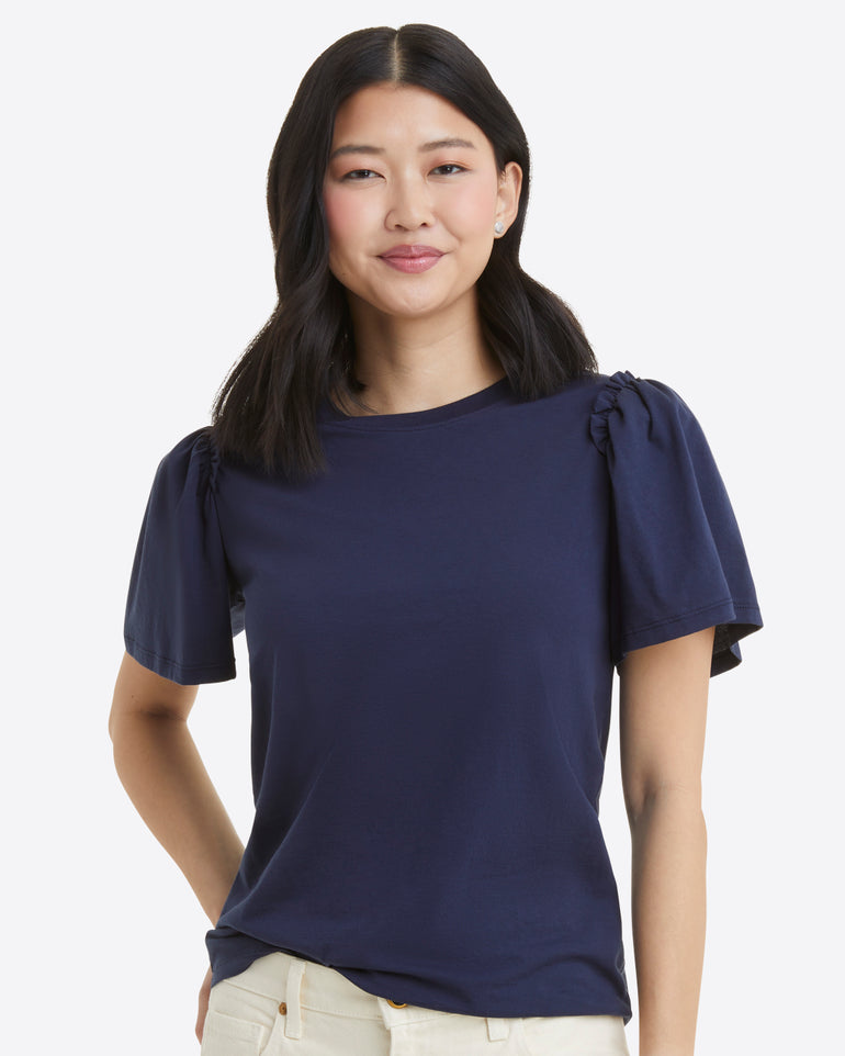 Wearing Draper James' navy Short Sleeve Easy Knit Top made of 100% Pima Cotton with butterfly sleeves, a person elegantly pairs it with light-colored pants against a plain background.
