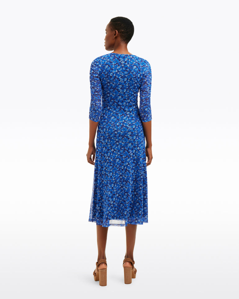 A person faces away, wearing the Draper James Selena V-Neck Midi Dress in Blue Scattered Ditsy with three-quarter sleeves and brown heels, set against a plain white background.