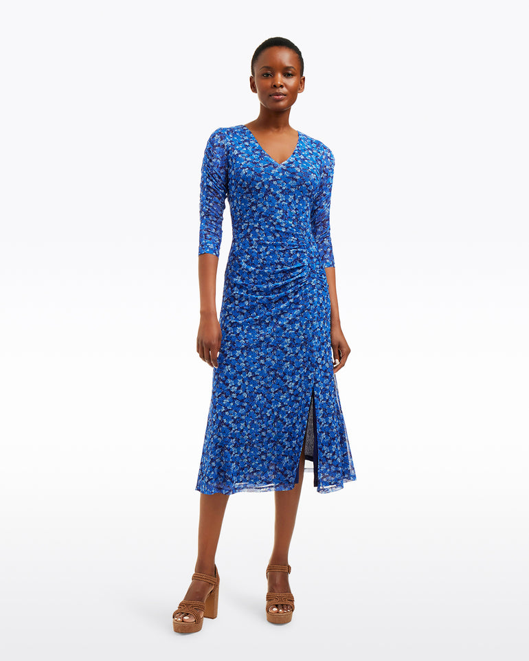 A person stands against a white background wearing the Draper James Selena V-Neck Midi Dress in Blue Scattered Ditsy with three-quarter sleeves, front slit, and brown platform sandals.