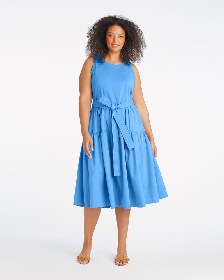 A woman stands against a white background wearing the Draper James Lila Mixed Media Midi Dress in Light Blue with a waist tie and tan sandals.