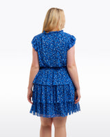A woman with blonde hair stands with her back to the camera, modeling the Draper James Alana Tiered Dress in Blue Scattered Ditsy against a plain white background.