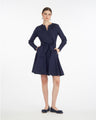 A woman stands against a white background wearing the Draper James Imogen Mini Shirtdressâ€”an effortless navy blue cotton work dress with long sleeves, a waist tie, and matching flats.