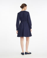 A woman stands facing away, wearing the Draper James Imogen Mini Shirtdress in navy cotton with a belted waist and matching navy flats, set against a plain white background.