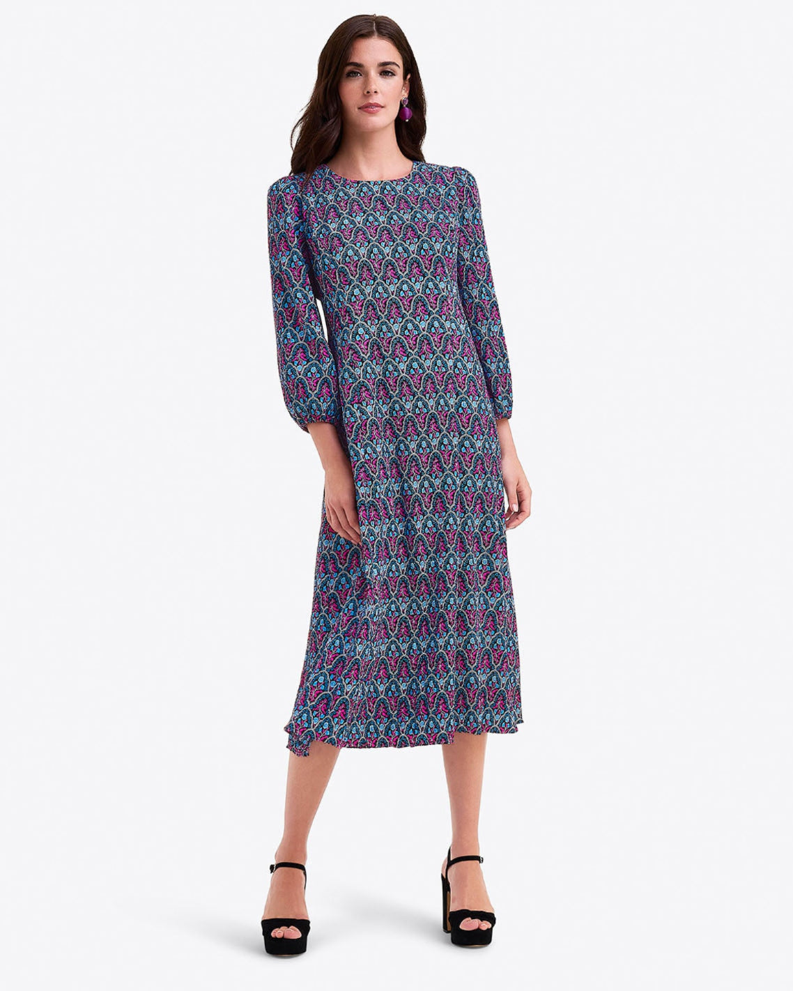 A woman wears the Draper James Long-Sleeve Midi Dress in blue and pink crinkle chiffon, featuring a crewneck and patterned design, standing with one hand by her side and the other near her hip, styled with black platform heels.