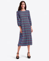 A woman wears the Draper James Long-Sleeve Midi Dress in blue and pink crinkle chiffon, featuring a crewneck and patterned design, standing with one hand by her side and the other near her hip, styled with black platform heels.