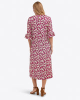 A woman faces away, wearing the Draper James Crewneck Midi Dress in Hammered Satin with ruffled sleeves and brown heeled sandalsâ€”machine wash cold for easy care.