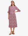 A woman models the Draper James Crewneck Midi Dress in Hammered Satin, featuring a maroon hue with white floral print and three-quarter ruffled sleeves, paired with brown ankle-strap sandals. Machine wash cold for best care.