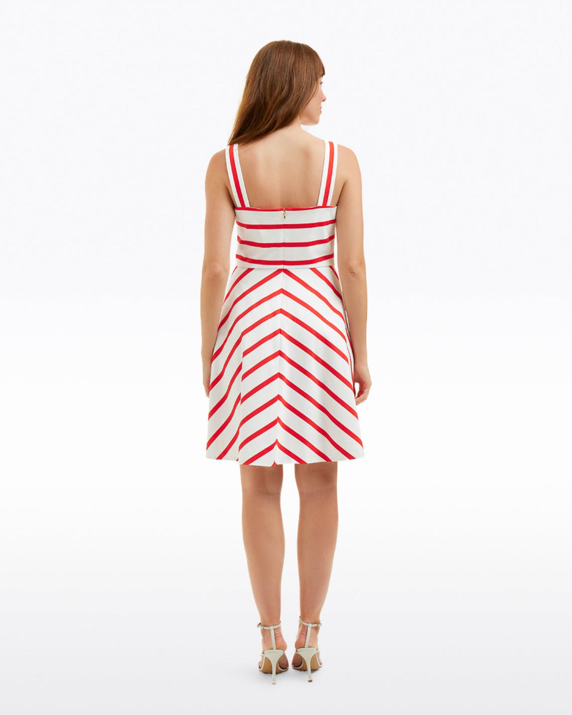 A woman stands facing away, wearing the Draper James Zoe Love Circle Dress in Red Wentworth Stripeâ€”a sleeveless cotton dress with chevron detailsâ€”paired with beige high-heeled sandals.