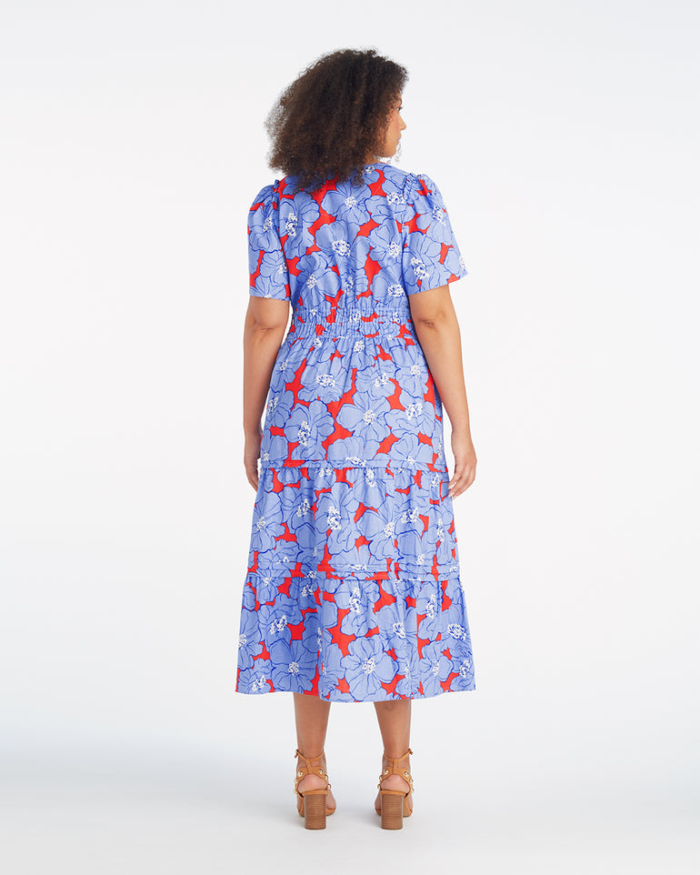 A woman faces away, wearing the Draper James Hollie Midi Dress in Floating Floral—a blue, red, and white cotton-linen dress with short sleeves—paired with brown platform sandals against a plain white background.