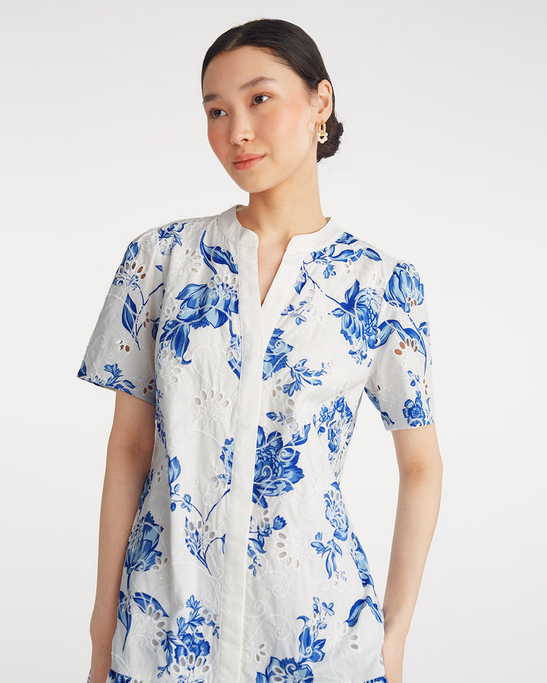 A woman wears the Draper James Molly Mini Dress in Magnolia Toile—100% cotton with blue floral print, short sleeves, and a v-neck—posing against a plain white background.