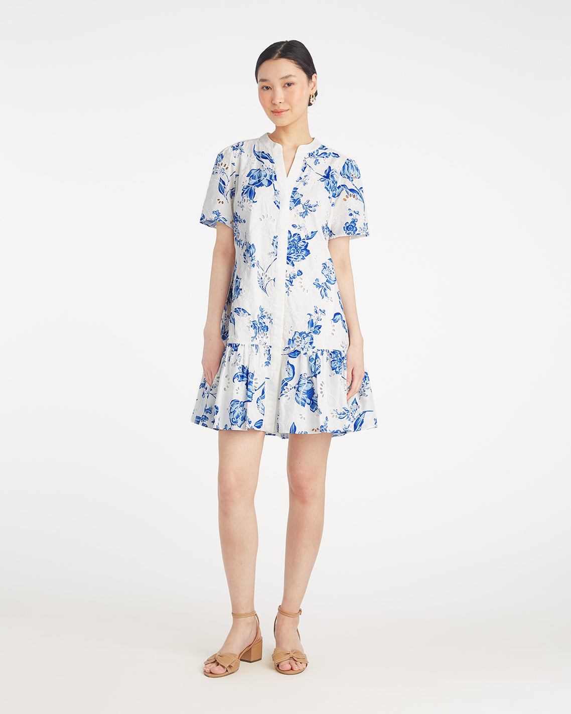 A woman stands against a white background wearing the Draper James Molly Mini Dress in Magnolia Toile, a short-sleeve, knee-length 100% cotton dress with blue magnolia patterns, paired with tan sandals.