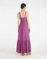 A woman faces away, wearing the Draper James Brynn Sleeveless Midi Dress in Amethyst—a fitted purple dress with a flared skirt—paired with tan sandals.