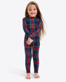 A child in Draper James' Kids Crewneck Pajama Set in Georgia Plaid stands barefoot, smiling with hands together against a plain background.