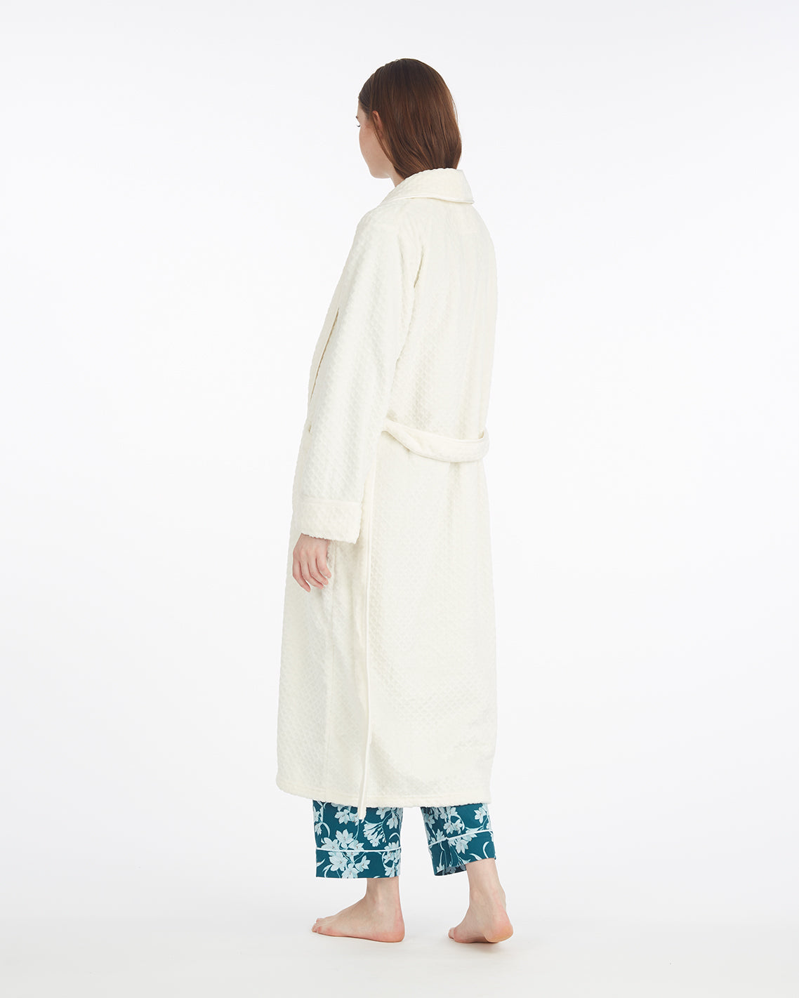 A person stands barefoot facing away, wearing the Draper James Shawl Collar Robe over teal floral pajama pants, set against a plain white background.