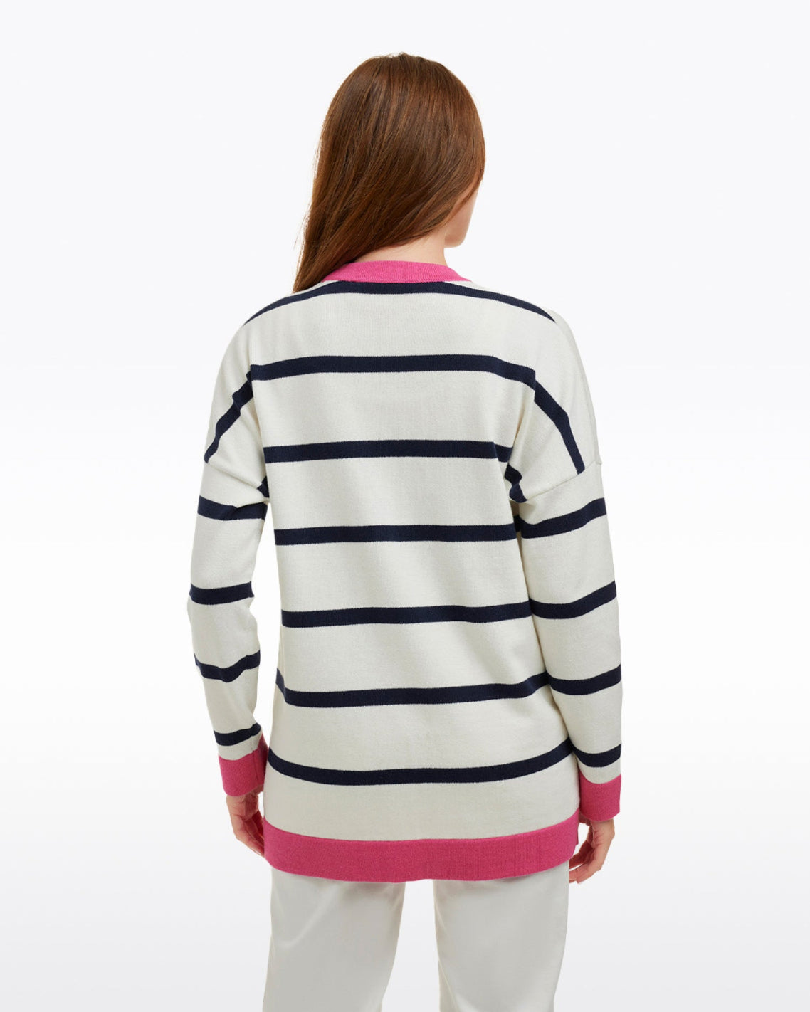 A woman with long brown hair is seen from behind, wearing the Draper James Cassadee Cardigan with black stripes and pink trim, paired with white pants against a plain background.