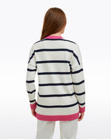 A woman with long brown hair is seen from behind, wearing the Draper James Cassadee Cardigan with black stripes and pink trim, paired with white pants against a plain background.
