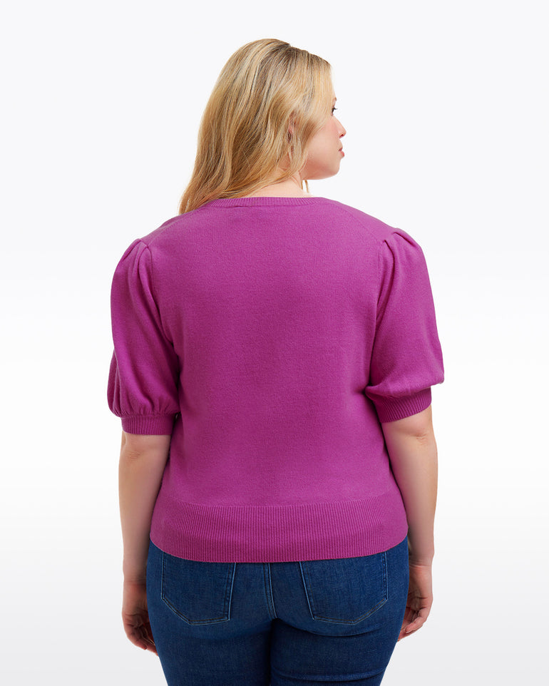 A woman with blonde hair is seen from the back wearing the Draper James Short Sleeve Cashmere Sweater in purple and blue jeans, set against a plain white background.
