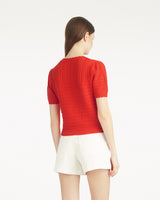 A woman with straight brown hair wears the Draper James Short Sleeve Pointelle Sweater in red and white shorts, standing with her back to the camera against a plain white background.